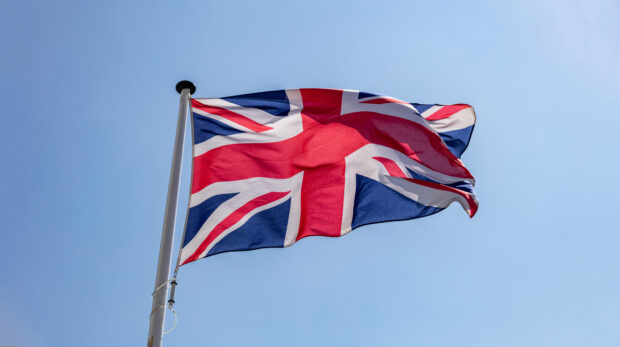 United Kingdom flag, Great Britain national symbol waving against clear blue sky, sunny day